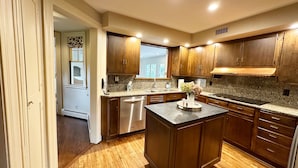 A modern kitchen with wooden cabinets, granite countertops, a stainless steel dishwasher, and a central island.