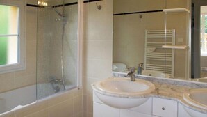 Un baño con ducha compartimentada por vidrio, dos lavamanos y un espejo.