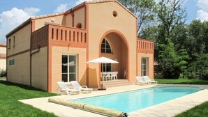 Una casa de dos pisos con piscina, un patio con sillas y un área de estar cubierta.