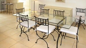 Un comedor con una mesa de vidrio rodeada de sillas de metal negro con cojines blancos.