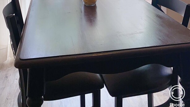 Un comedor con una mesa y sillas, una ventana con cortinas, y vistas a un patio trasero con árboles y una cerca.