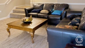 Una sala de estar con un sofá de cuero negro, una mesa de centro de madera y una lámpara de pie.