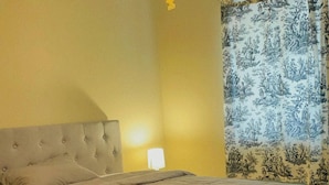 Un dormitorio con una cama grande, una mesita de noche, una lámpara y una ventana con cortinas estampadas.