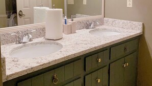 Un baño con dos lavamanos, un espejo grande y armarios verde oscuro con tiradores dorados.