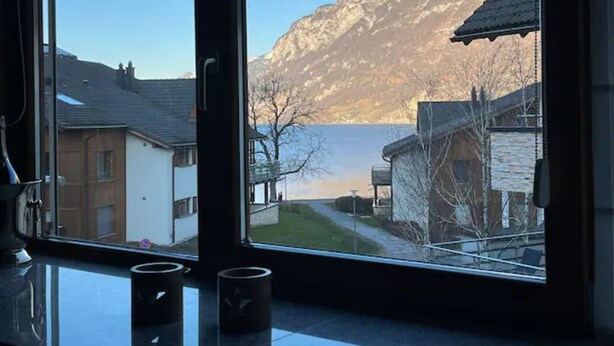 Una habitación con un amplio ventanal con vista a un lago y montañas.