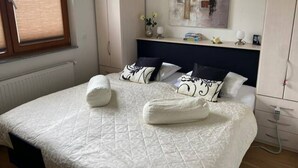 Una cama bien hecha con almohadas y una manta, una mesita de noche con un florero y un cuadro en la pared.