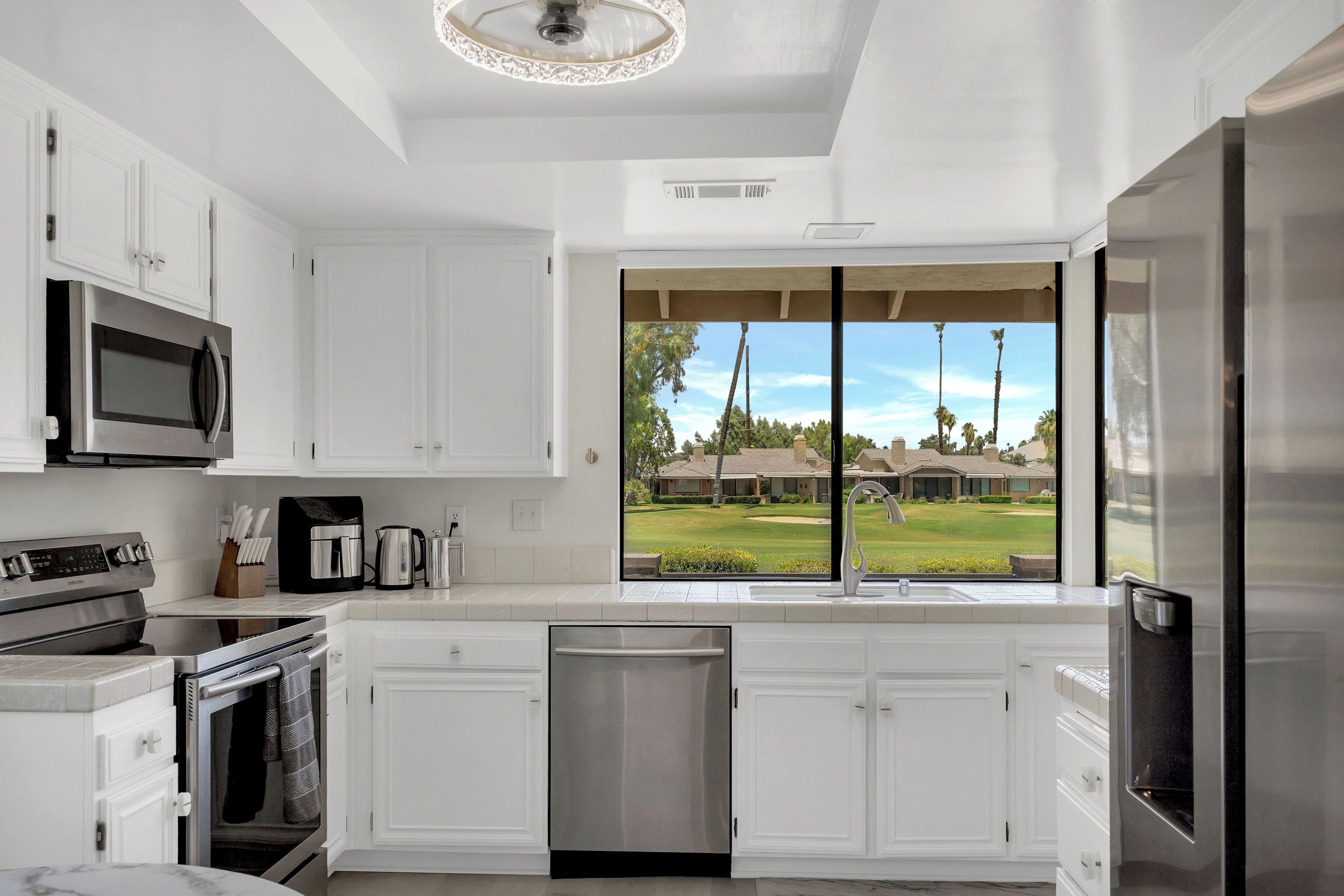 A modern kitchen with white cabinetry, stainless steel appliances, and a large window offering a view of a golf course.