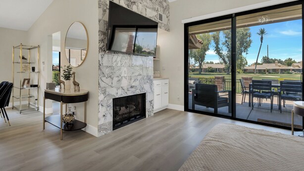 A modern living room with a stone fireplace, a large mirror, and a view of the outdoors through a sliding glass door. - Modern Desert Retreat (Palm Desert)