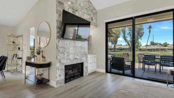A modern living room with a stone fireplace, a large mirror, and a view of the outdoors through a sliding glass door.