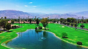 A golf course with a pond, palm trees, and mountains in the background. - Modern Desert Retreat (Palm Desert)