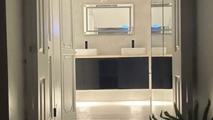 Corridoio che conduce a un bagno con uno specchio, un lavandino e una pianta in vaso.