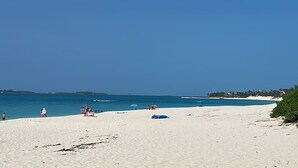 Una spiaggia con cielo sereno, una riva sabbiosa e alcune persone.