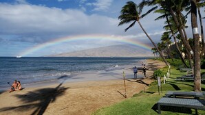 A beach with a rainbow, palm trees, and a boat in the distance. - Top Floor Beachfront Condo with Ocean view (Kihei)