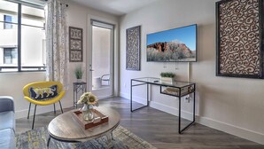 A modern living room with a large window, a round coffee table, a yellow chair, and a TV on the wall. - King Beds-Walk Score 81 & Parking 3047 (Scottsdale)