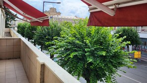 A balcony with red awnings, a tiled floor, and a view of a building with a clock tower in the background. - Proche Centre Ville, Appartement Pour 6 Voyageurs Comprenant 3 Suites (Châlons-en-Champagne)