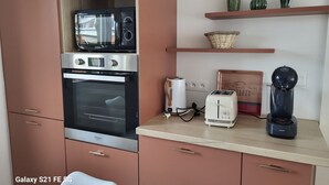 A kitchen with a built-in oven, microwave, toaster, and coffee maker. There are shelves with decorative items and a wicker basket. - Proche Centre Ville, Appartement Pour 6 Voyageurs Comprenant 3 Suites (Châlons-en-Champagne)