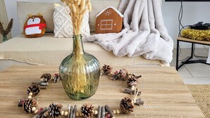 A cozy living room with a sofa, a decorative vase with dried plants, and a gingerbread house decoration. - Proche Centre Ville, Appartement Pour 6 Voyageurs Comprenant 3 Suites (Châlons-en-Champagne)