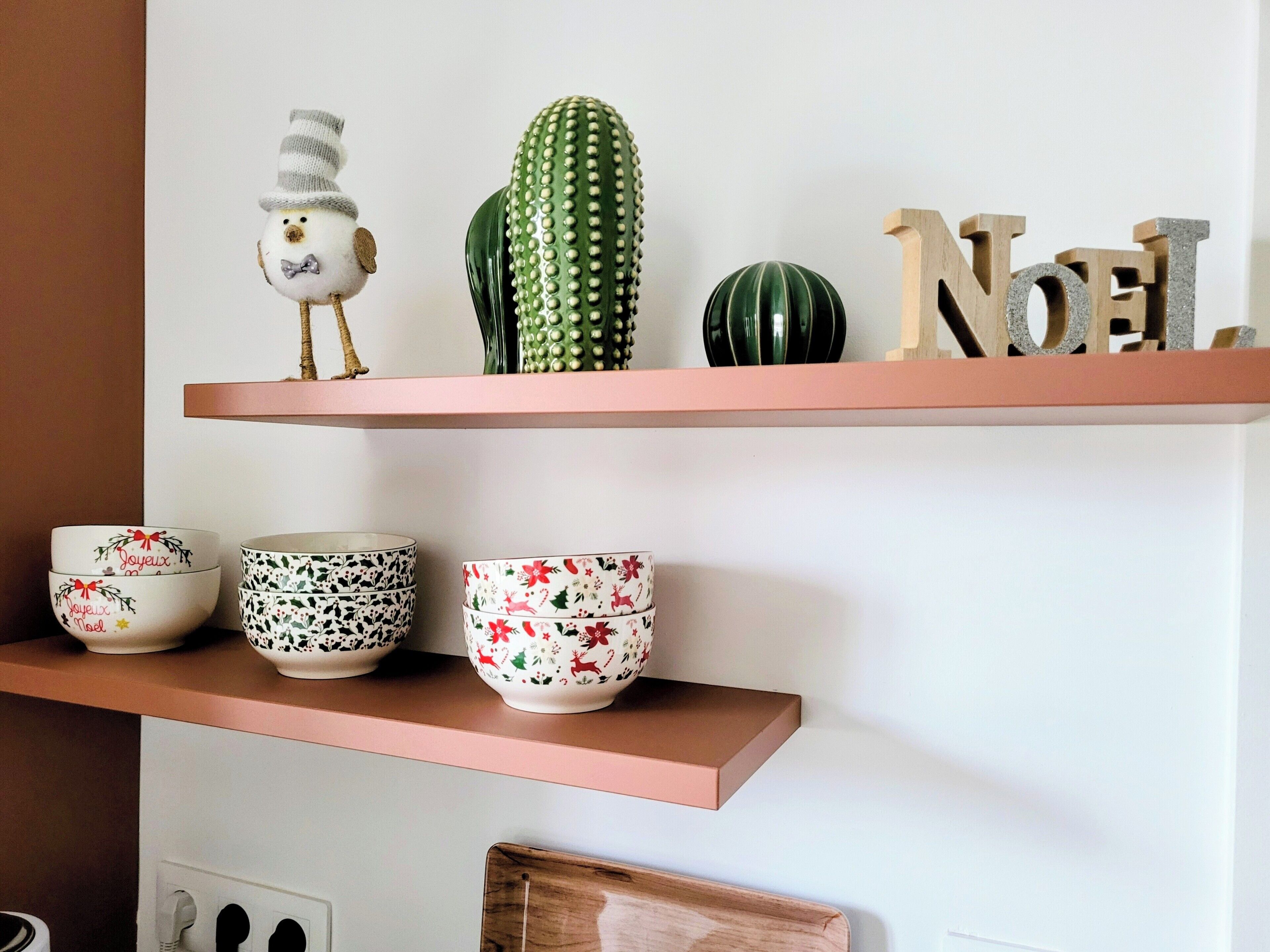Una estantería de cocina con objetos decorativos, incluyendo un cactus, una figurita de pájaro y cuencos con motivos festivos.