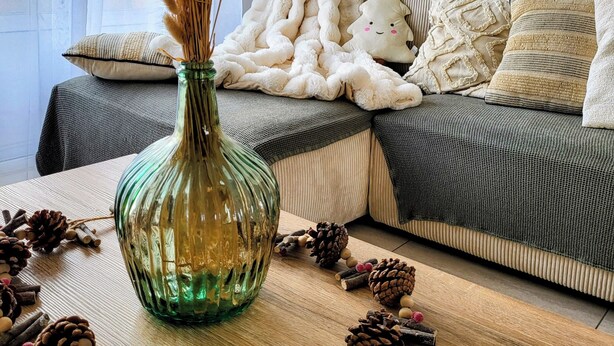 A cozy living room with a sofa, a decorative vase with dried plants, and a wooden table with pinecones and a green glass vase. - Proche Centre Ville, Appartement Pour 6 Voyageurs Comprenant 3 Suites (Châlons-en-Champagne)
