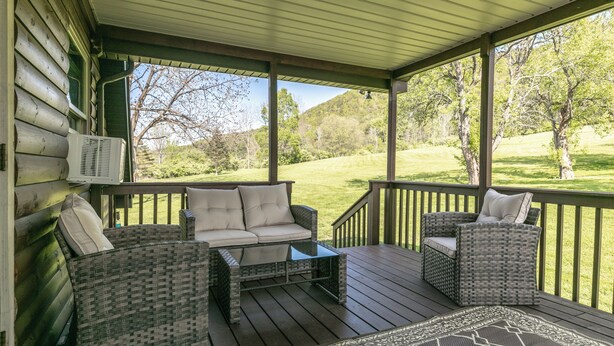 A covered porch with wicker furniture, a glass table, and a view of a grassy landscape. - Creekside Cabin - Watkins Glen, Corning, Finger Lakes with Hot Tub (Corning)