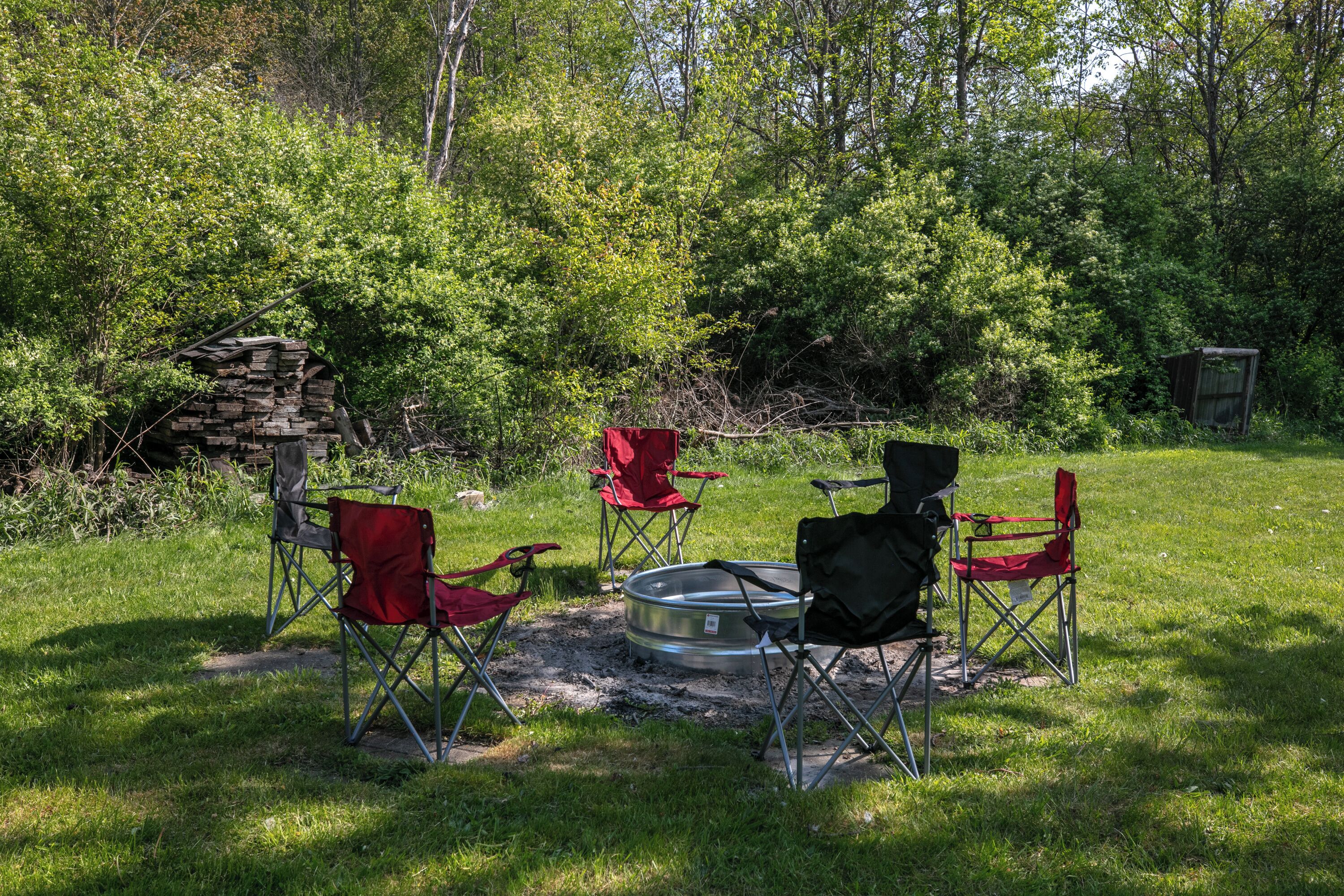 Un terrain de camping avec un foyer circulaire entouré de quatre chaises pliantes, dont une est rouge.