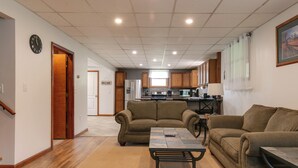 A spacious living area with a sofa set, a coffee table, and a kitchen in the background. - Creekside Cabin - Watkins Glen, Corning, Finger Lakes with Hot Tub (Corning)