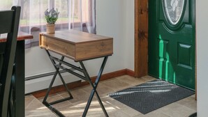 A room with a wooden desk, a chair, a potted plant, a green door, and a window with sheer curtains. - Creekside Cabin - Watkins Glen, Corning, Finger Lakes with Hot Tub (Corning)
