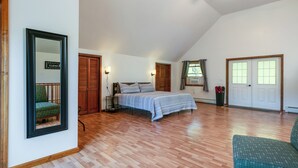 A spacious room with a large bed, wooden flooring, a ceiling fan, and a view of the outdoors through a window. - Creekside Cabin - Watkins Glen, Corning, Finger Lakes with Hot Tub (Corning)