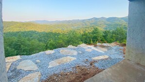 Vista desde un balcón con un sendero de piedra que conduce a una cadena montañosa boscosa.
