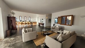Un'ampia zona giorno con cucina moderna sullo sfondo, un tavolo da pranzo con sedie e un'ampia finestra che fa entrare luce naturale.