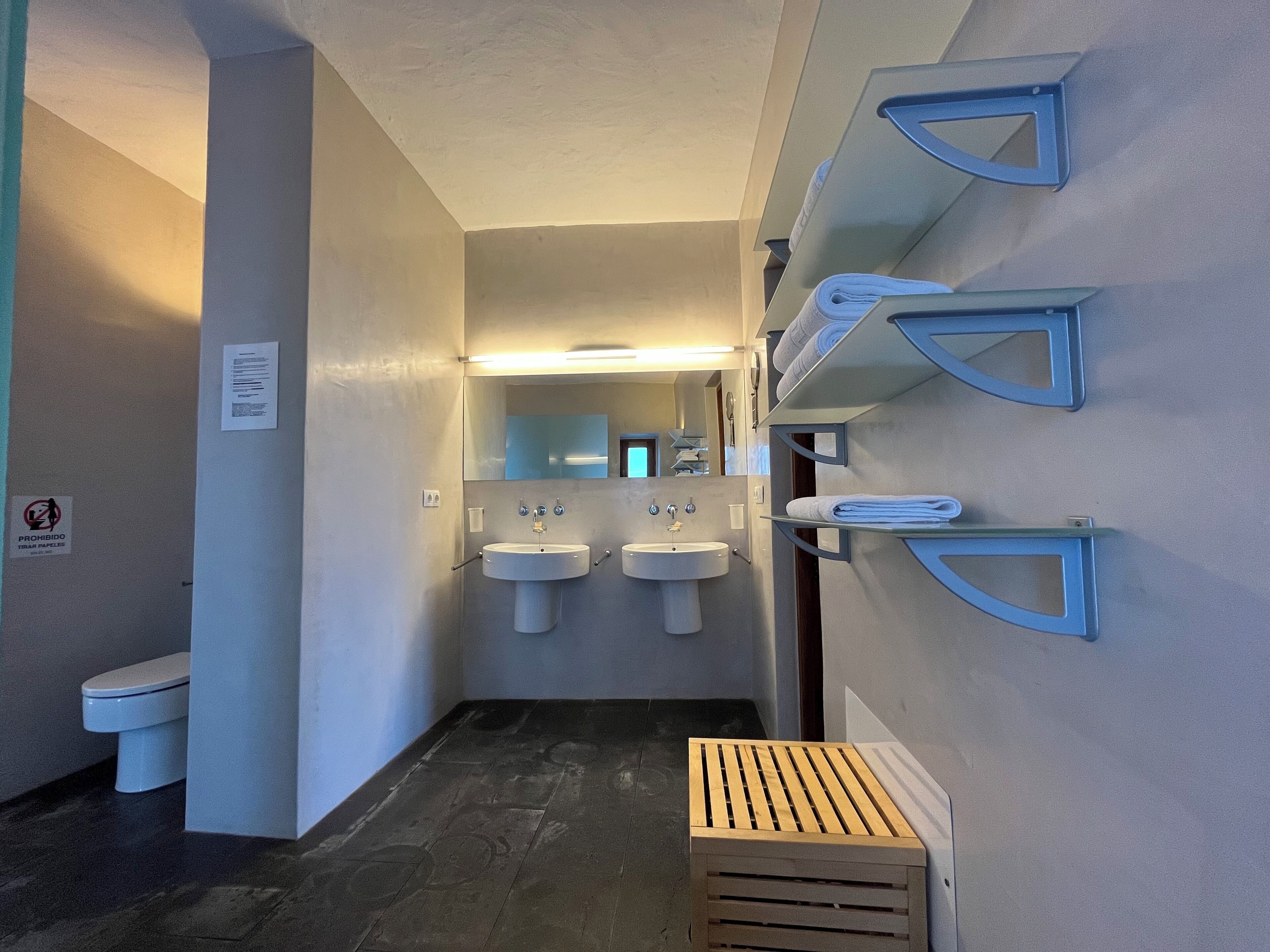 Un baño moderno con dos lavamanos, un inodoro y un banco de madera.