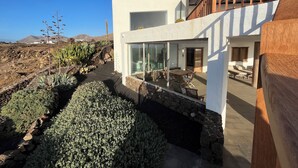 Una casa moderna con facciata in vetro, terrazza in legno e muro di sostegno in pietra.