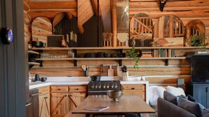 A rustic kitchen with wooden cabinets, a stove, and a dining area with a table and chairs. - Teanaway Pines: Riverfront Mountain Retreat (Cle Elum)
