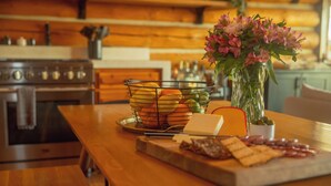 A wooden kitchen table with a fruit basket, a vase of flowers, and a charcuterie board. - Teanaway Pines: Riverfront Mountain Retreat (Cle Elum)