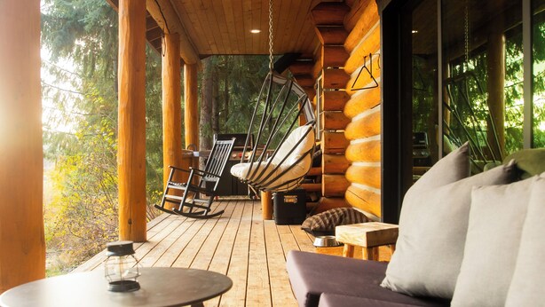 A wooden deck with a sofa and chairs, a table, and a hanging chair. - Teanaway Pines: Riverfront Mountain Retreat (Cle Elum)