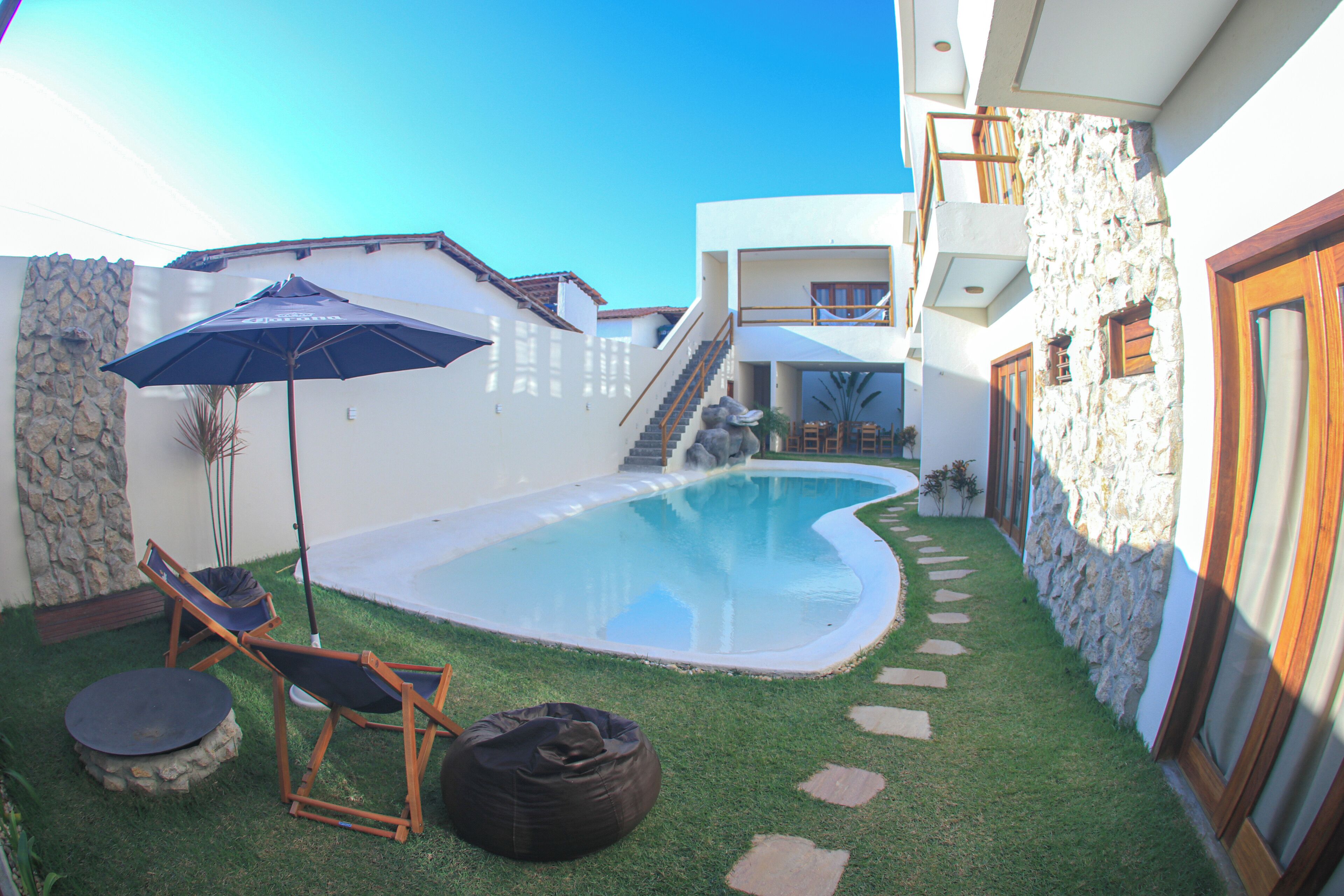 Une piscine bordée d’un muret en pierre, avec une terrasse en bois et un parasol bleu.