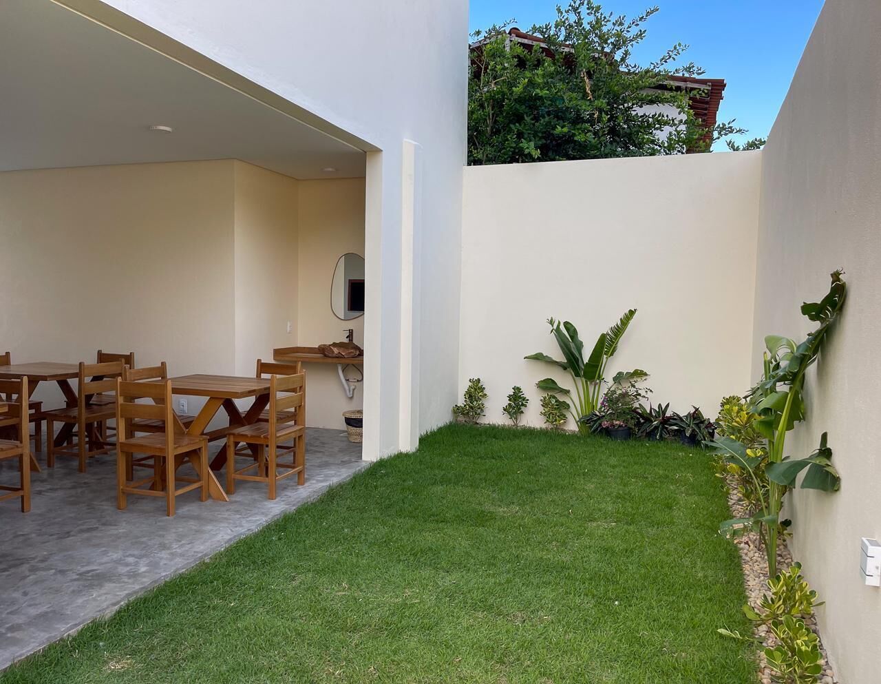 A patio with a dining table and chairs, a small lawn, and various plants.