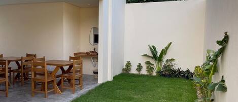 A patio with a dining table and chairs, a small lawn, and various plants.