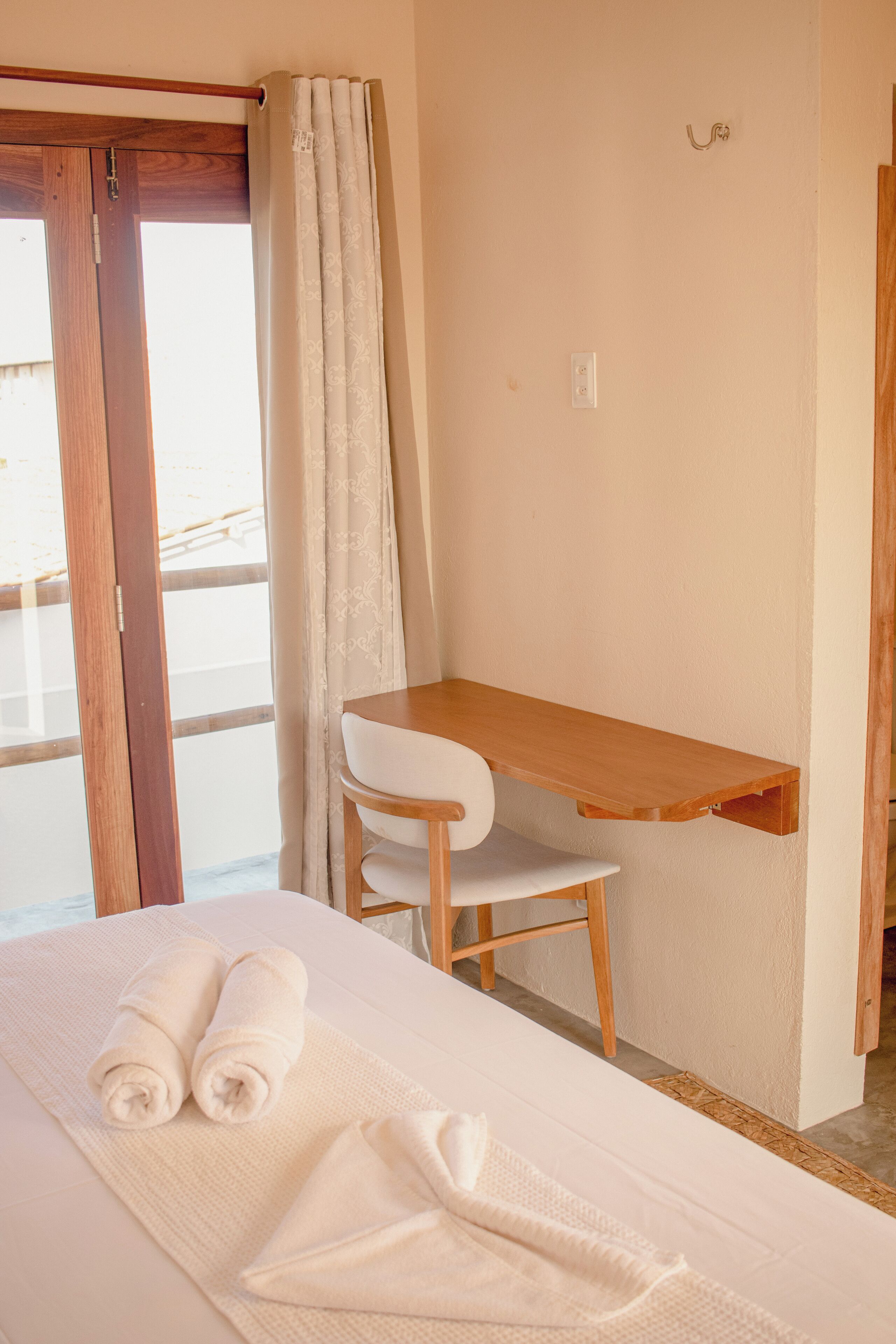 A bedroom with a bed, a wooden desk, a chair, and a window with curtains.