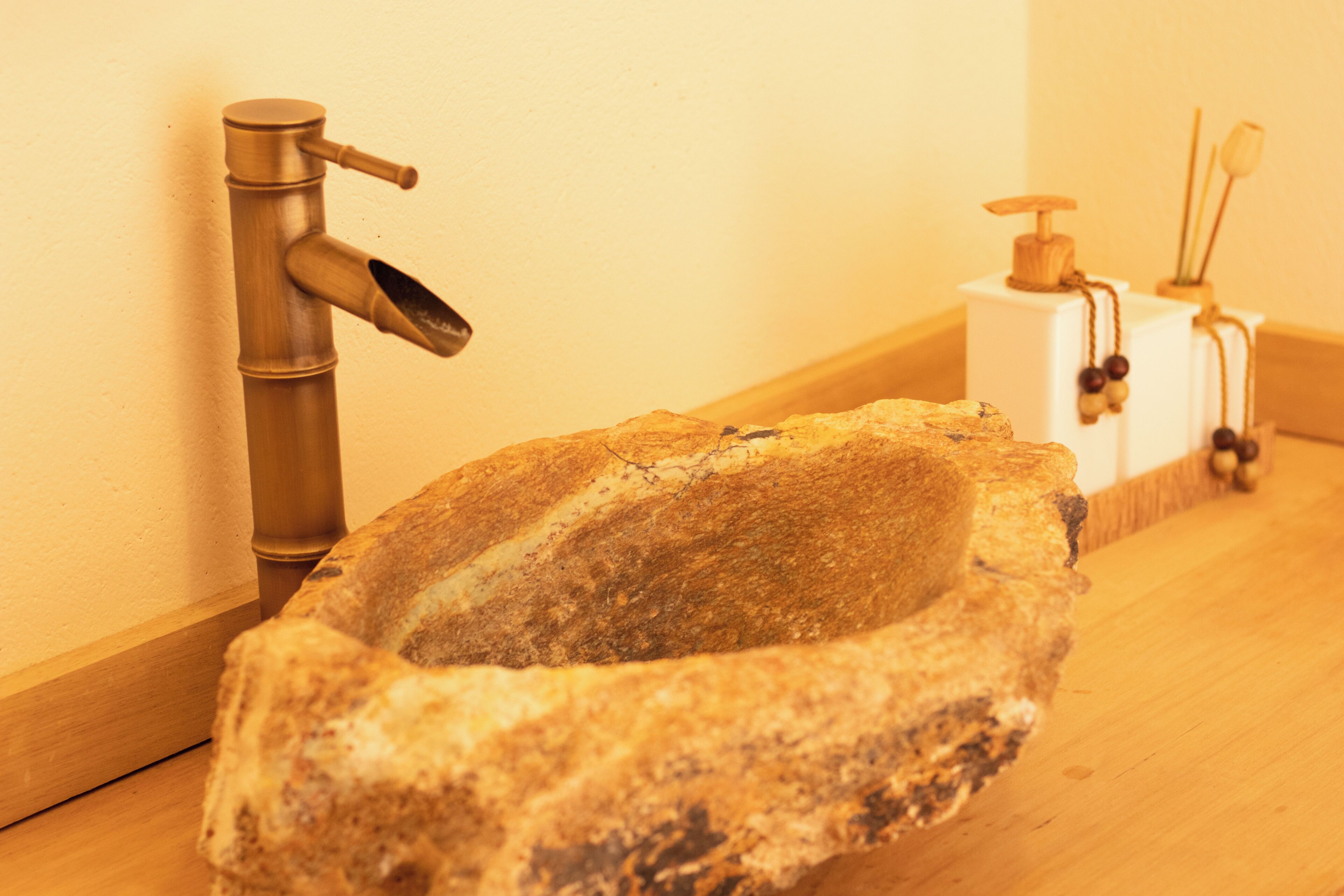 A stone sink with a brass faucet, a soap dispenser, and a wooden soap dish.