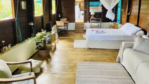 A cozy cabin-style room with a bed, a chair, a small table, and a window. - Bungalow Avec vue Dans Lieu Calme (Le Carbet)