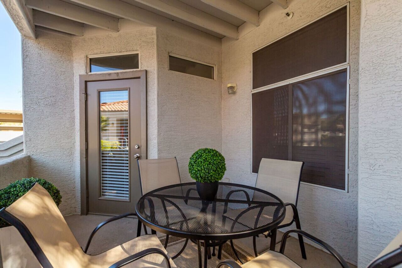 A patio with a round table, chairs, a potted plant, and a door with blinds.