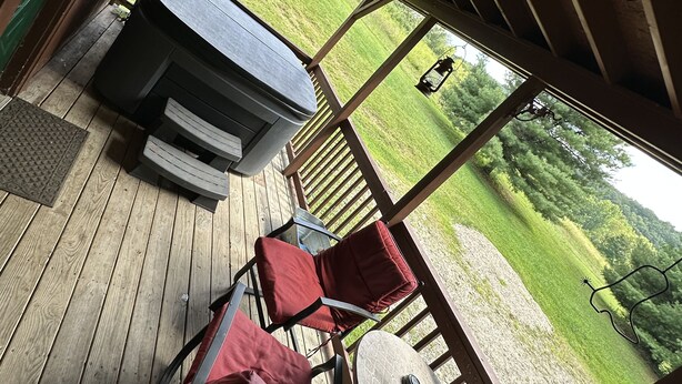 A covered outdoor deck with a grill, a table, and red chairs.