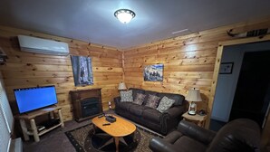 A cozy living room with a wooden interior, a fireplace, a television, and a leather armchair.