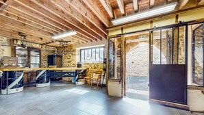 A rustic interior with exposed wooden beams, stone walls, and a large window overlooking a stone courtyard. - Cozy home in Neuilly le Vendin with WiFi (Neuilly le Vendin)