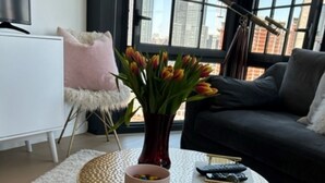 A modern living room with a round, textured coffee table, a vase with tulips, a remote control, and a book on a white rug. - Gorgeous apt for Labor Day weekend.  View of Manhattan at Greenpoint 



 (Brooklyn)