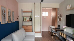 En moderne stue med en grå sofa, trægulv, et fjernsyn og et skrivebord med en bærbar computer.