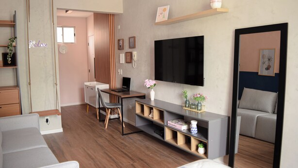 En moderne stue med et fladskærms-tv, en sofa, et skrivebord med stol og en reol.
