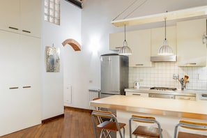A modern kitchen with white cabinets, a stainless steel refrigerator, a gas stove, and pendant lighting.