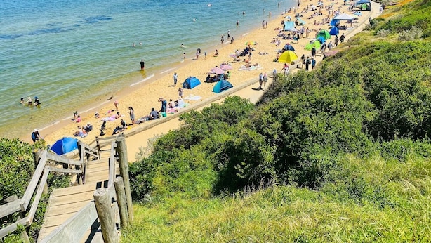 Ein Strand mit Menschen, Zelten und einer Holzpromenade.